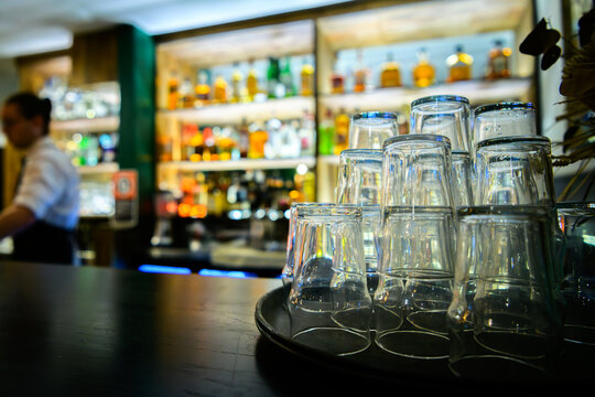 A warm, inviting bar setting captured in soft focus, showcasing gleaming glasses stacked on a tray against a backdrop of colorful spirits, creating a cozy atmosphere.