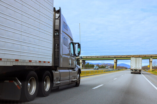 Two trucks drive on highway with grass trees nearby bridge is visible in South Carolina