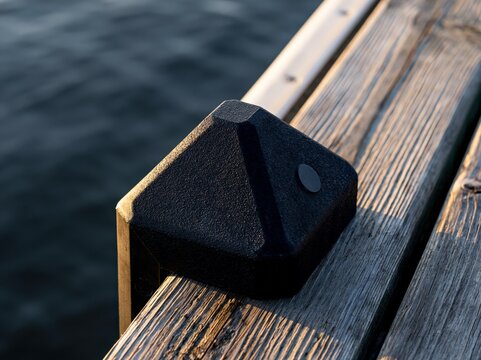 Black plastic dock bumper corner guard on wooden dock at water edge with single directional light