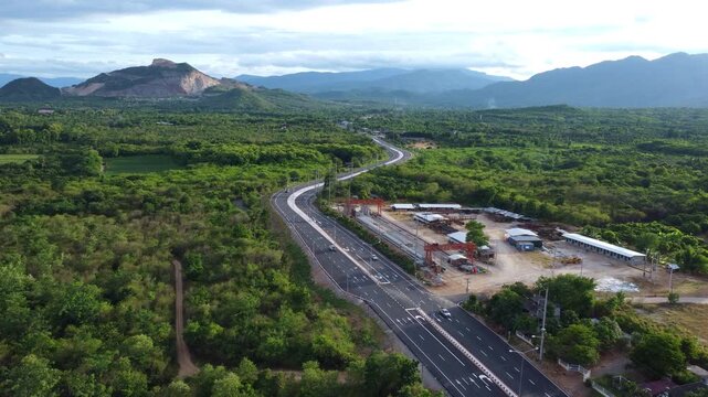 Aerial drone view of cars driving on country asphalt road bend surrounded by green forest and mountains