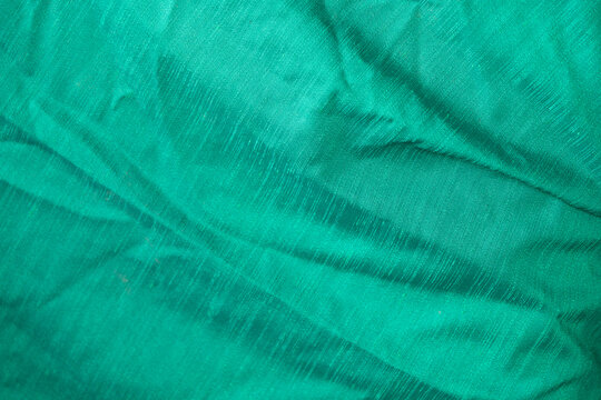 Full frame texture of emerald green wrinkled cotton fabric.A high-resolution texture shot of a crumpled emerald green or teal cotton fabric surface. The image highlights the natural weave.