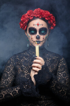 Halloween beauty portrait of woman with burning candle in hands. Beautiful female face with Santa Muerte makeup. Eyes closed.