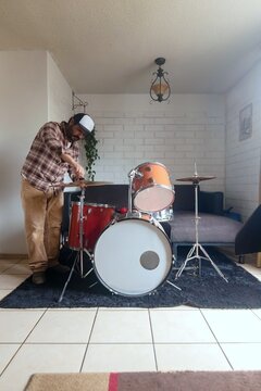 A man gets ready to practice a percussion instrument at home, an acoustic drum set