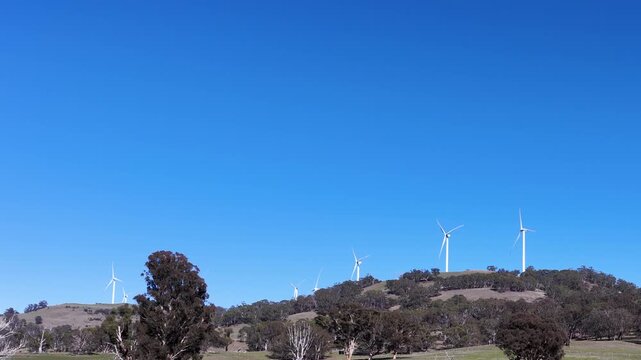 Wind Turbines Rotating on a Grassy Hillside Under Clear Blue Sky