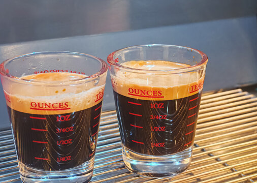 freshly brewed espresso shots served in transparent measuring glasses on a coffee machine tray. Suitable for coffee culture, barista preparation, cafe, beverage industry, and culinary concepts.