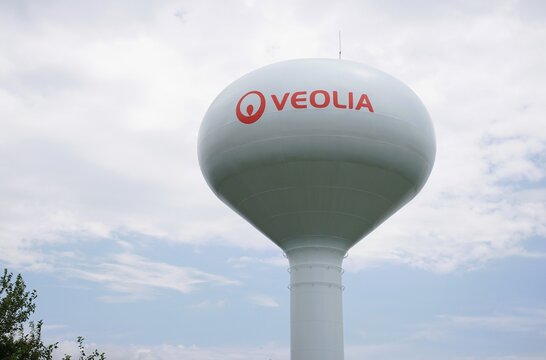 New Castle County, Delaware, U.S.A - Aug 2, 2026 - A large white Veolia water tower featuring red branding stands prominently against a light, cloudy blue sky.