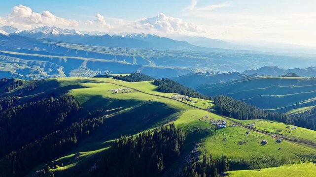 Aerial view of green alpine meadows, yurt camps on the ridge and distant snow-capped mountains in Kalajun Grassland, Ili, Xinjiang, China.