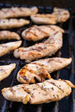 Vertical close-up photo of seasoned chicken strips cooking on a barbecue grill with shallow depth of field.