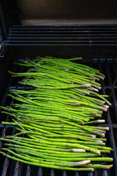 Vertical photo of fresh green asparagus spears cooking on an outdoor barbecue grill.