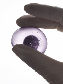 Transparent Purple Bioactive Capsule Held by Gloved Hand for Biotechnology and Skincare Research