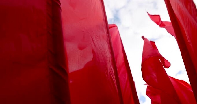 Red textile flags on a dark flagpole in the wind, a close view of the red flags fluttering under the bright daytime sky