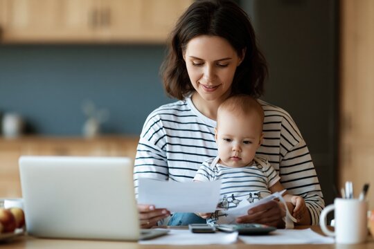 Mother multitasking with baby while working on laptop and reviewing home finance