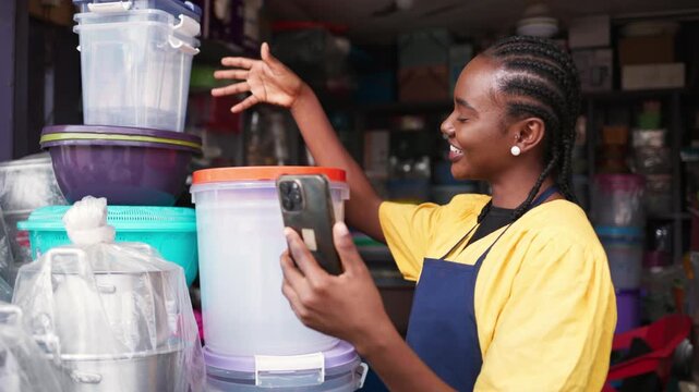 African woman small business owner smiling and talking on a video call on her smartphone in her shop