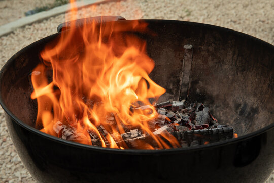 Fire blazes in charcoal grill, illuminating backyard setting. Cooking and socializing concept