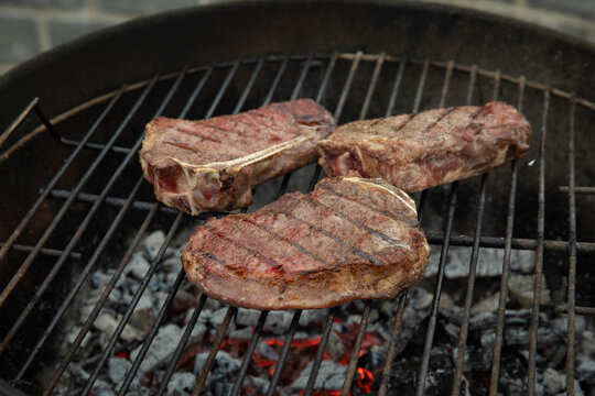 Steaks sizzle on grill as flames dance below charcoals. Cooking and outdoor dining concept