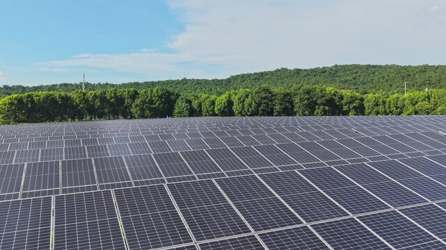 Drone flying forward over a solar farm surrounded by trees