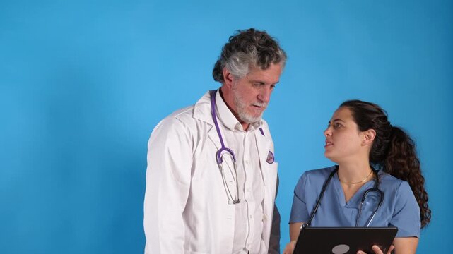 Senior male physician and female nurse reviewing digital records on a tablet in studio. Concept for medical teamwork, hospital staff collaboration, healthcare technology, and consultation.