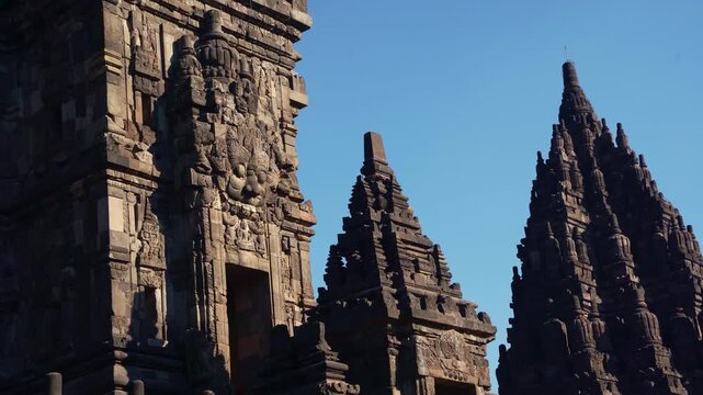 Prambanan Temple spires rise dramatically between carved stone walls beneath a vivid blue sky in Yogyakarta, Indonesia.