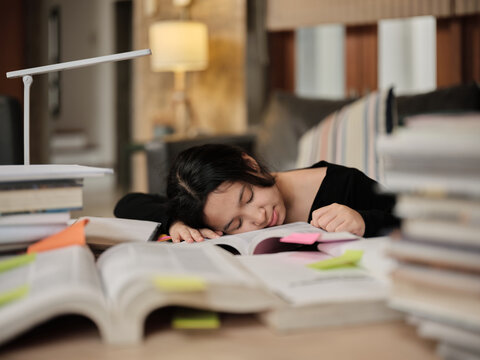 College Asian teenage girl tired and burned out from overwhelmed study pile of books, stressed learning at home with pile of textbooks, reading and writing for school exam, homeschooling education.