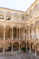 Fototapeta premium Majestuoso patio interior de un palacio histórico con arcos de medio punto, columnas clásicas, balaustradas de piedra y un carruaje tradicional decorativo