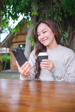 Vertical portrait image of a woman holding mobile phone and coffee cup in the outdoors