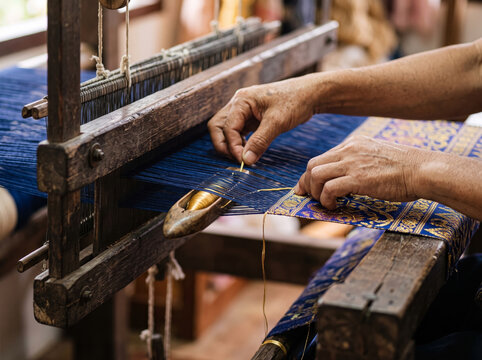 Weaver operating traditional wooden handloom to weave textile fabric threads