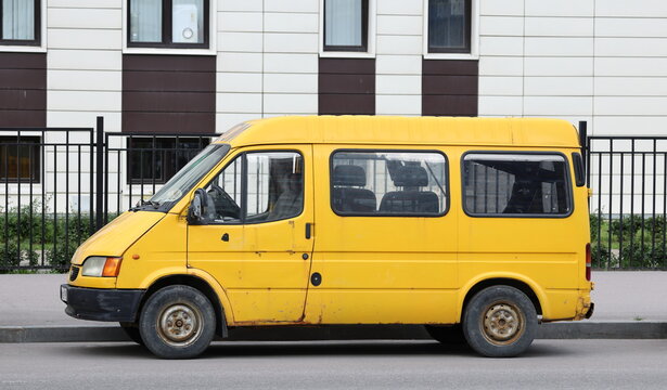 An old yellow minibus is parked on the road near the sidewalk