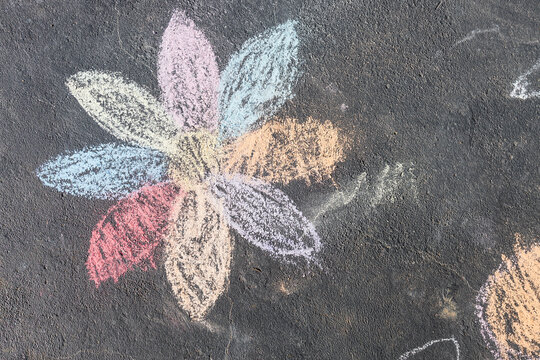child's drawing of daisy with rainbow petals with concrete chalks on driveway