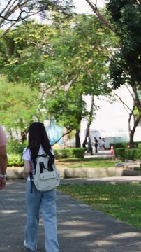 Asian Female Student with Backpack Walking Through Sunny University Campus Park