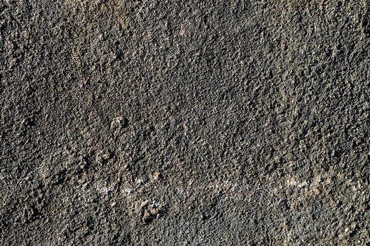 The texture of this asphalt surface is rough and dark, featuring small stone granules. It resembles rough, granular asphalt or concrete, with a dark gray or black color.