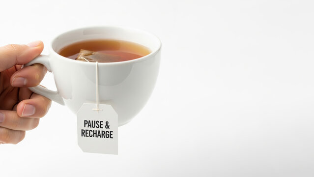 Mental Health Workplace Concepts. Close up of a hand holding white ceramic cup with tea bag label pause and recharge on white background for relaxation and break