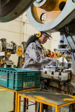 Female machine operator in hard hat and ear muffs leaning over a power press die checking tooling on the factory floor