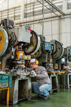 Male engineer crouching beside a row of power presses inside a tall industrial hall glancing over the die assembly