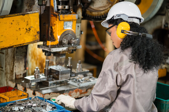 Female machine operator bending over a power press die sorting stamped metal parts into a bin on the factory floor