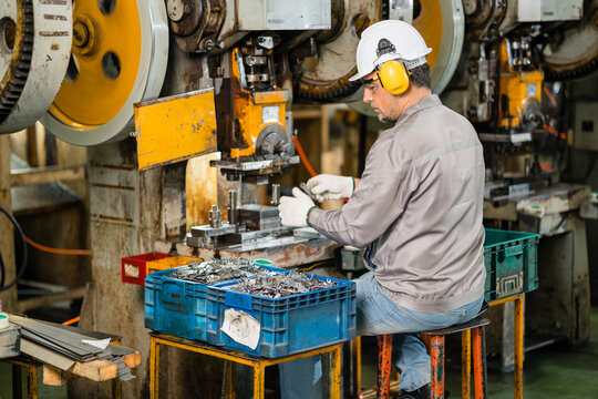 Male machine operator sorting freshly stamped metal parts with gloved hands beside a row of mechanical power presses on factory floor