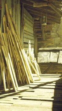 Sunlight streams into an aged building, casting shadows on wooden planks. Stacks of wooden sticks lean against the weathered walls, creating a serene and nostalgic atmosphere.