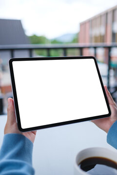 Vertical mockup image of a woman holding digital tablet with blank white desktop screen in cafe