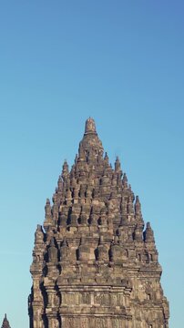 Ornate upper tower of Prambanan Temple rises prominently against a bright cloudless sky in Central Java, Indonesia.