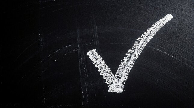 White chalk check mark drawn on black chalkboard. Symbol of approval and completion. Simple clear graphic sign for success or correct answer.