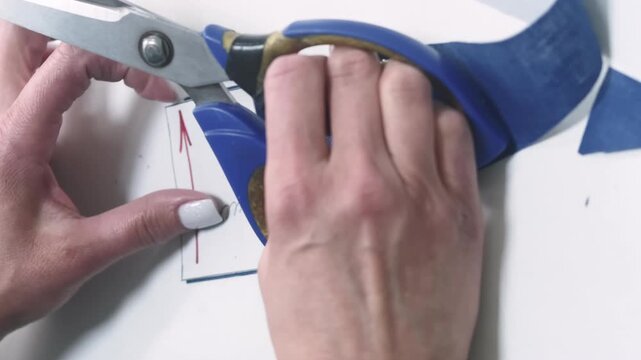 Vertical video. Cutting garment. Tailor process. Professional female hand creating clothes according to paper draft working with scissors on white table.