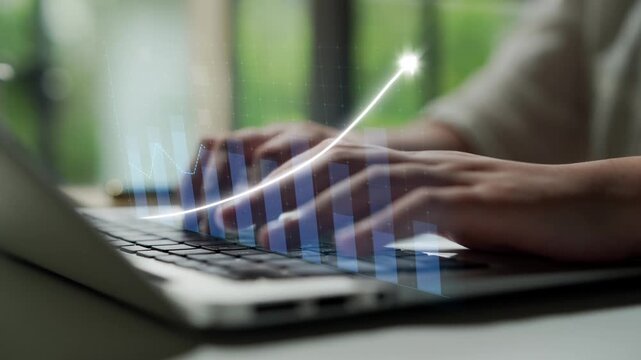 A close-up view of hands typing on a laptop surrounded by a digital stock market graph, symbolizing growth and success in a modern office space. Copula