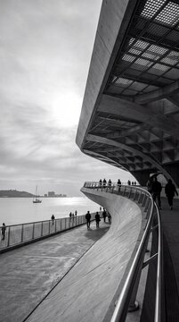 Striking black and white view of a modern curved waterfront building and promenade with pedestrians strolling