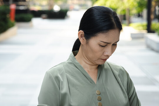 senior asian woman in a green park looking down with sorrowful face