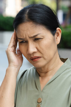 sick asian senior woman suffering from headache on one side of her head, holding temple in pain