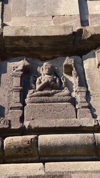Ancient seated deity relief carved into a weathered stone niche on the sacred facade of Prambanan Temple in Central Java.