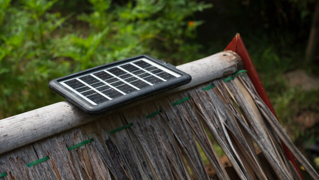 A small solar panel attached to an old, weathered wooden surface, possibly part of outdated machinery, against a greenery backdrop.