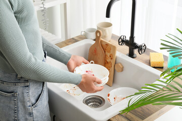 Womans hands holding dirty dishes over a kitchen sink with cutting boards and a sponge, household...