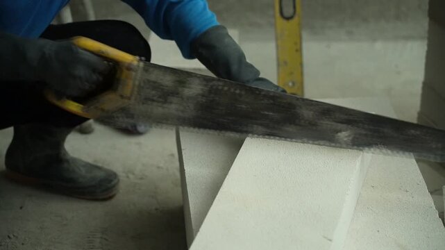 Construction worker cutting AAC lightweight concrete block using a hand saw.
