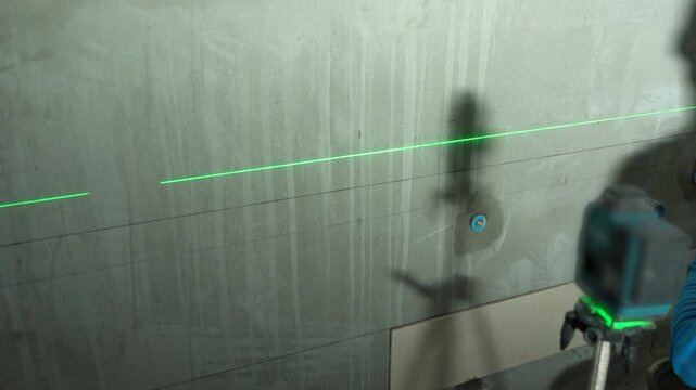 Professional green beam laser level projector projecting leveling lines on a wall.