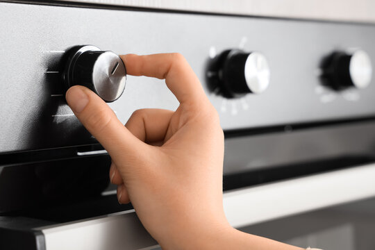 Female hand adjusting built-in oven in kitchen, closeup